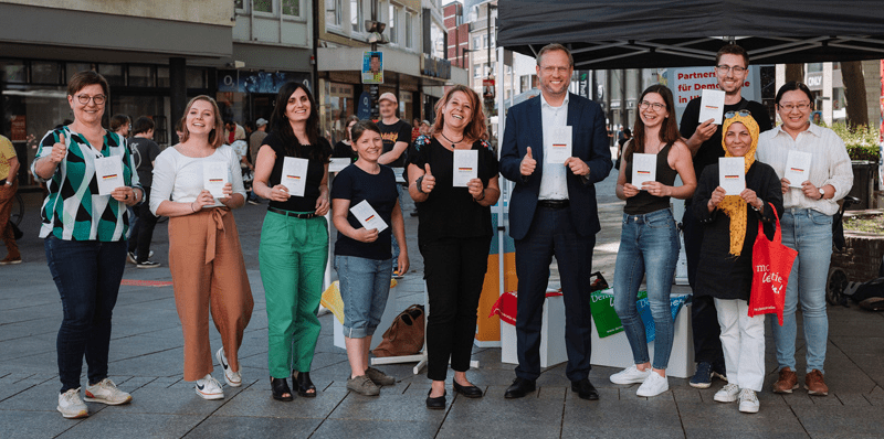 Mitarbeiterinnen und Mitarbeiter der Stadt Ulm sowie von "Jugend aktiv" präsentieren in der Fußgängerzone kleine Bücher mit dem Grundgesetz.